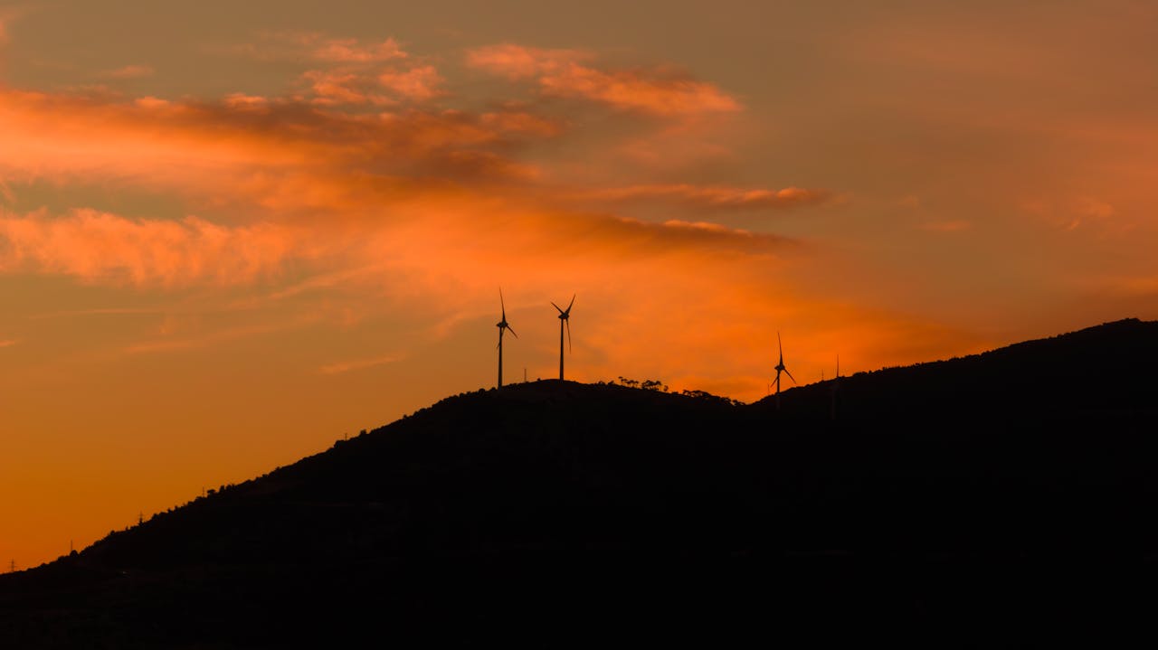 Silhouetted wind turbines during a vivid sunset in Çeşme, Türkiye, highlighting renewable energy.